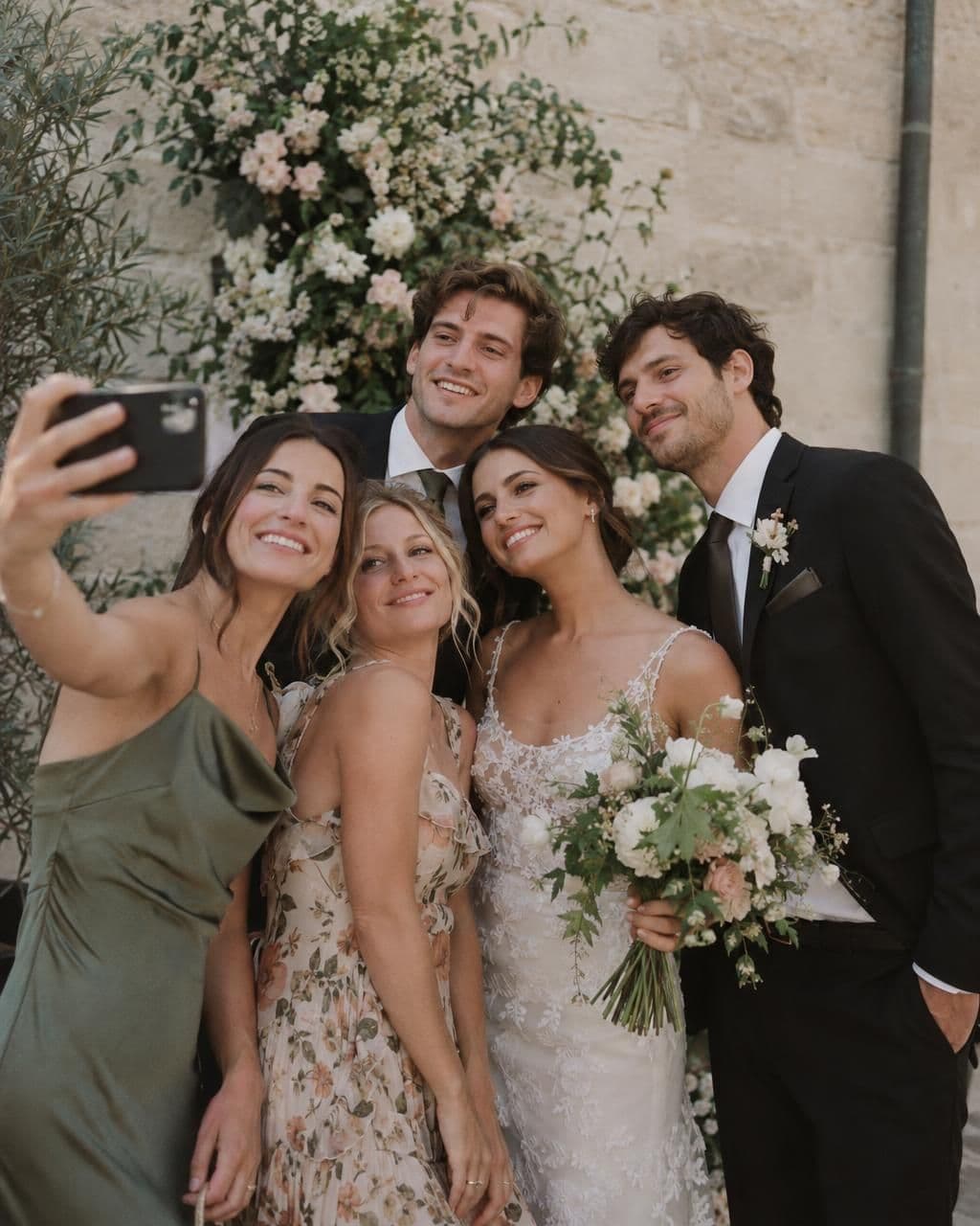 Friends posing together in front of a floral wall at a wedding